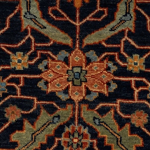 May include: Close-up of a navy blue rug with an intricate floral pattern. The design features a central flower in shades of orange and green, surrounded by detailed motifs in blue, orange, and green. The rug's background is a deep navy blue.