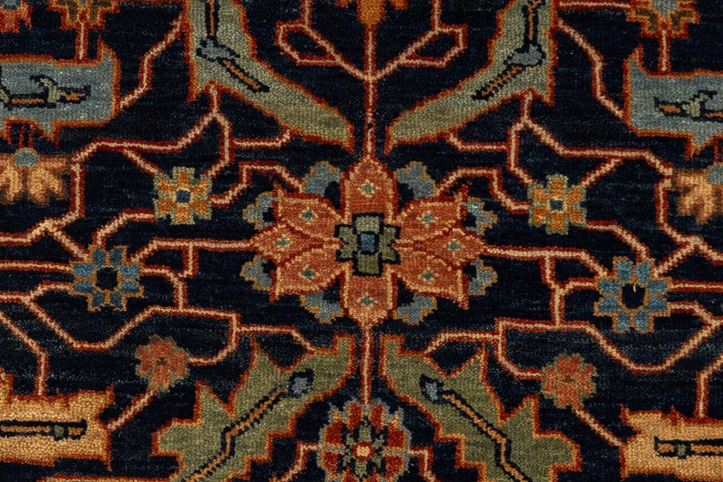 May include: Close-up of a navy blue rug with an intricate floral pattern. The design features a central flower in shades of orange and green, surrounded by detailed motifs in blue, orange, and green. The rug's background is a deep navy blue.