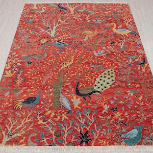 Puede incluir: Una alfombra roja con un patrón detallado de árboles, flores y pájaros. La alfombra presenta un pavo real con una cola azul y verde.