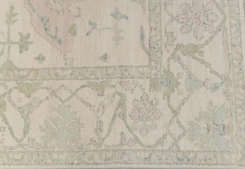 May include: A beige rug with a floral pattern in shades of pink and green. The rug has a border with a repeating design.