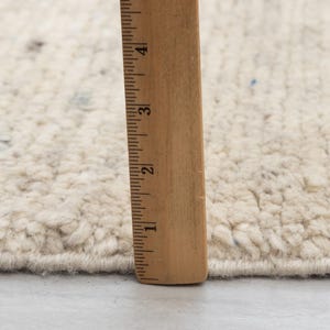 May include: Close-up of a white rug with a ruler measuring 4 inches. The rug has a textured, fluffy surface.