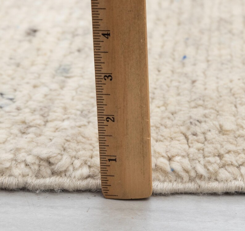 May include: Close-up of a white rug with a ruler measuring 4 inches. The rug has a textured, fluffy surface.