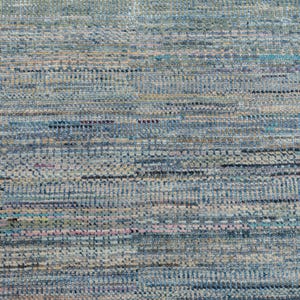 May include: Close-up of a textured rug with a mix of blue, gray, and beige hues. The rug's design features horizontal and vertical lines, creating a woven appearance. The color palette includes hints of teal and pink.