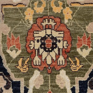 May include: Detailed close-up of a rug with a central floral design in shades of rust, cream, and black, set against a green and tan backdrop. The rug features intricate patterns and a dark blue border with yellow floral accents.