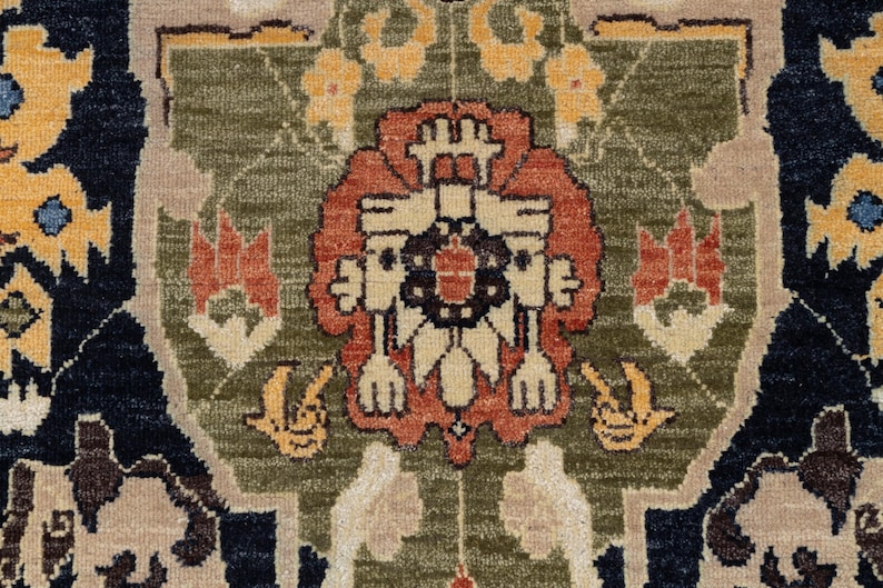 May include: Detailed close-up of a rug with a central floral design in shades of rust, cream, and black, set against a green and tan backdrop. The rug features intricate patterns and a dark blue border with yellow floral accents.