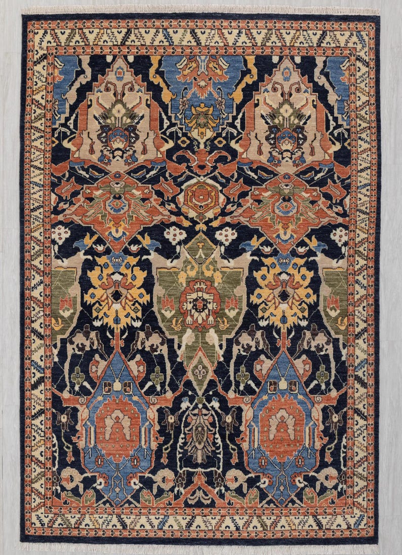 May include: A rectangular rug with a detailed, symmetrical pattern. The rug has a navy blue base with designs in orange, beige, blue, and green. The border is a lighter beige with a repeating geometric design. The rug is suitable for a living room.