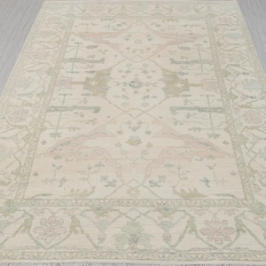 Op de afbeelding: Een beige vloerkleed met een traditioneel Perzisch ontwerp in tinten roze, groen en bruin. Het kleed heeft een gedetailleerde rand met bloemmotieven.