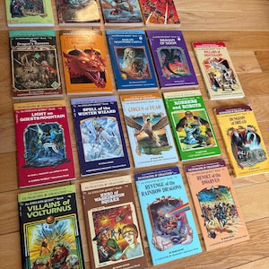 May include: A collection of vintage "Dungeons & Dragons" adventure books. The covers feature colorful illustrations of dragons, wizards, and fantasy scenes. Titles include "Return to Brookmere," "Dragon's Ransom," and "Revolt of the Dwarves."