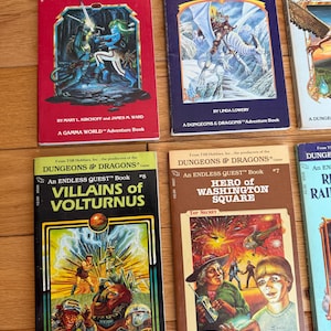 May include: A collection of vintage "Dungeons & Dragons" adventure books. Titles include "Light on Quests Mountain," "Spell of the Winter Wizard," "Villains of Volturnus," and "Hero of Washington Square." The books feature colorful fantasy illustrations and text.