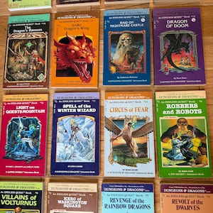 May include: A collection of vintage "Dungeons & Dragons" adventure books. The covers feature fantasy illustrations of dragons, wizards, and other mythical creatures. Titles include "The Dragon's Ransom," "Under Dragon's Wing," and "Dragon of Doom."