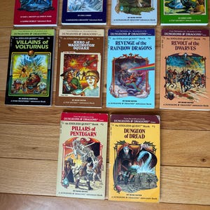May include: A collection of vintage "Dungeons & Dragons" adventure books. The covers feature colorful illustrations of fantasy scenes, including dragons, wizards, and warriors. Titles include "Light on Quests Mountain" and "Dungeon of Dread."
