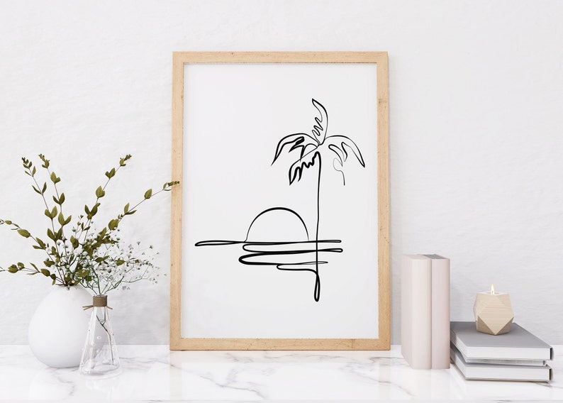 Puede incluir: Un dibujo en blanco y negro de una palmera y una puesta de sol sobre el agua, enmarcado en un marco de madera clara.