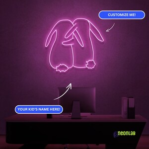 May include: Pink neon sign with two bunnies hugging each other. The sign says "Customize Me!" and "Your Kid's Name Here!" at the top and bottom of the sign.