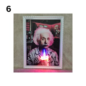 May include: A framed print of Albert Einstein holding a lit candle in a dimly lit room. The print is in a white frame with a silver border.