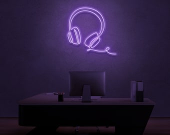 May include: Purple neon sign of headphones with a cord extending to the right. The sign is mounted on a dark purple wall above a desk with a computer monitor and a stack of folders.