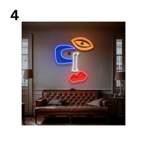 May include: A neon light sculpture depicting a stylised face with a blue eye, orange eye, and red lips. The sculpture is mounted on a wall in a room with a brown leather sofa.