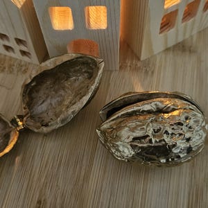 Puede incluir: Dos mitades de cascanueces decorativas, doradas y ornamentadas, una abierta y otra cerrada, sobre una superficie de madera.