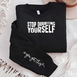 Könnte beinhalten: Schwarzer Pullover mit dem Text "Stop Doubting Yourself" auf der Vorderseite und "You got this" auf dem Ärmel.