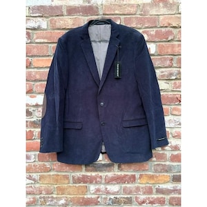 May include: A navy blue corduroy blazer featuring two front buttons, two flap pockets, and brown elbow patches. The interior lining has a grey and white checkered pattern. A black brand tag reading Harvé Benard is attached to the lapel.