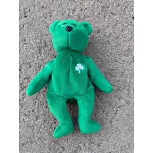 May include: A green plush bear with a black nose and a white shamrock on its chest. The bear is made of soft material and has a classic teddy bear design. The bear is a St. Patrick's Day themed item.