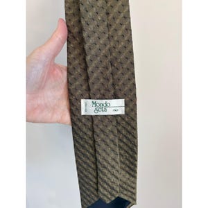 May include: A brown silk tie with a geometric pattern. The tie has a label that reads "Mondo Seta ITALY". The tie is made of 100% silk.