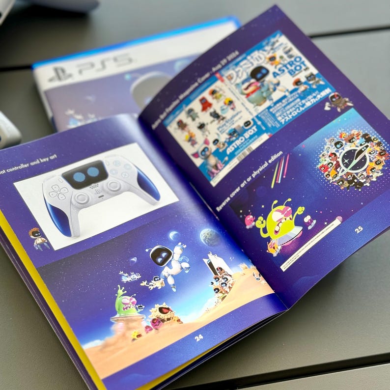 May include: An open book with a blue and yellow cover. The book features illustrations of a video game character, a controller, and a spaceship. The text on the cover reads "ASTRO BOT".