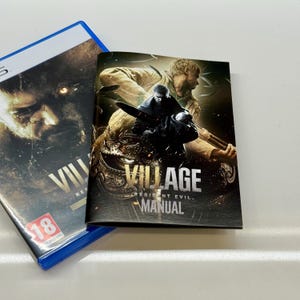 May include: A PS5 game case and manual for "Resident Evil Village." The game case is blue with a dark image of a face and the word "VILLAGE." The manual features a dark image of characters and the game title.
