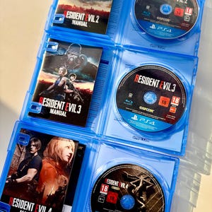 Peut inclure: Trois bo&icirc;tiers bleus ouverts de jeux vid&eacute;o Resident Evil, r&eacute;v&eacute;lant des disques et des manuels. Les jeux sont Resident Evil 2, 3 et 4. Les disques noirs pr&eacute;sentent des illustrations de jeux et le logo Capcom.