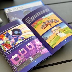 May include: An open book with a blue cover and colorful illustrations. The book features a robot character and a purple and pink landscape with a series of pink squares with eyes. The text on the page reads "Weird and wonderful secret levels are also scattered across the galaxy!"