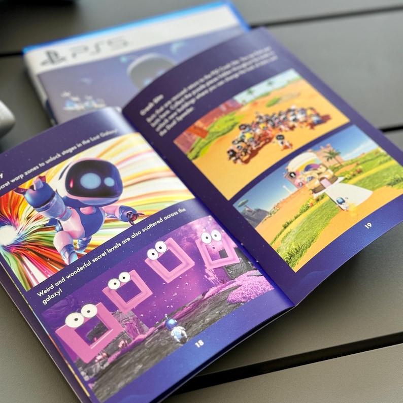 May include: An open book with a blue cover and colorful illustrations. The book features a robot character and a purple and pink landscape with a series of pink squares with eyes. The text on the page reads "Weird and wonderful secret levels are also scattered across the galaxy!"