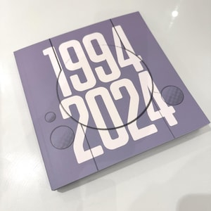 Op de afbeelding: Een lavendelkleurige boekomslag met de witte tekst "1994 2024" en een cirkelvormig ontwerp. De omslag heeft twee kleine, cirkelvormige, getextureerde details. Het ontwerp is eenvoudig en modern.