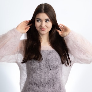 Könnte beinhalten: Eine Frau trägt einen hellrosa Strickpullover mit lockerer Passform und langen Ärmeln. Der Pullover hat eine zarte, luftige Textur.
