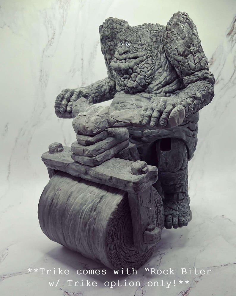May include: A grey stone figure of a creature riding a stone roller, with the text "**Trike comes with "Rock Biter w/ Trike option only!**" below.