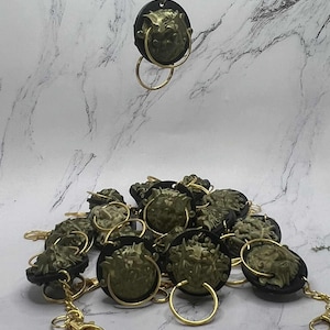May include: Keyrings with a lion's head design. Each keyring has a gold-coloured chain and ring, with a dark circular backing. The lion's head is a muted green colour.