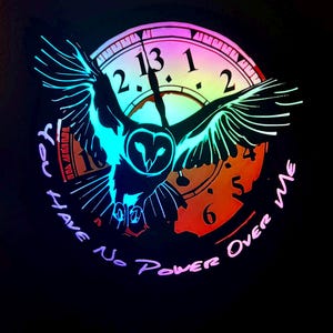 May include: A black graphic featuring a glowing owl with outstretched wings, superimposed over a clock face. The clock has the numbers 1, 2, 5, 6, and 13 visible. The text "You Have No Power Over Me" is written around the owl.
