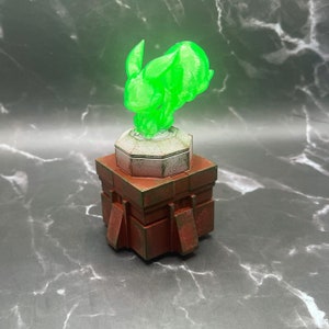 May include: A green, 3D printed, rabbit-like creature with a white base sits atop a brown, rectangular, 3D printed pedestal.