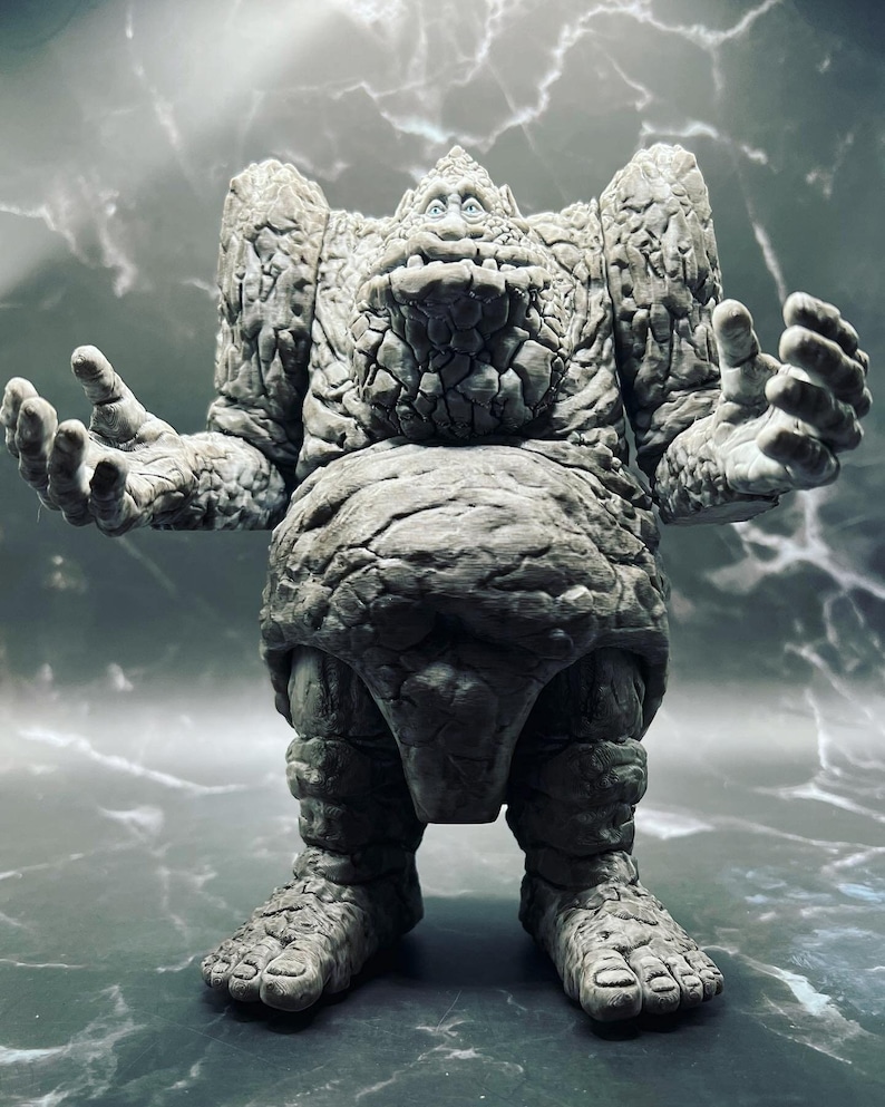 May include: A grey stone figure with a humanoid shape and a large, cracked head. The figure has two arms outstretched and two legs with large feet. The figure appears to be made of rock and has a rough, textured surface.