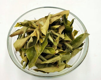 May include: A glass bowl filled with dried curry leaves. The leaves are a light green color and have a slightly brown hue.