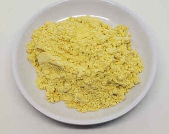 May include: A small white bowl filled with a generous amount of bright yellow mustard powder.