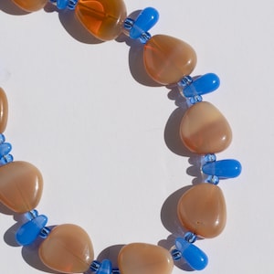 May include: A necklace featuring large, rounded, peach-colored beads interspersed with bright blue, teardrop-shaped beads. The necklace is strung on a clear cord, creating a striking contrast between the colors and shapes. A unique piece of jewelry.