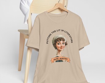Könnte beinhalten: Beiges T-Shirt mit einem Porträt von Jane Austen und dem Text "Putting the Lit in Literature". Das Design beinhaltet ein Banner mit "Jane Austen". Eine weiße Baseballkappe liegt auf einem Holzstuhl.