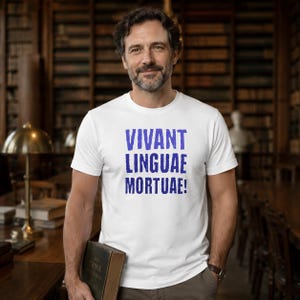 May include: A white short-sleeved t-shirt featuring the blue text VIVANT LINGUAE MORTUAE! printed in a bold, distressed font across the chest. The garment has a classic crew neckline and a straight hem, providing a clean and simple appearance.