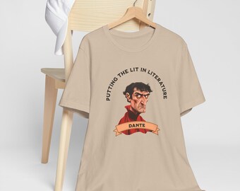 May include: Beige t-shirt with a graphic of Dante Alighieri, the Italian poet, wearing a red collar. The text "PUTTING THE LIT IN LITERATURE" surrounds the image. A white baseball cap rests on a wooden chair.