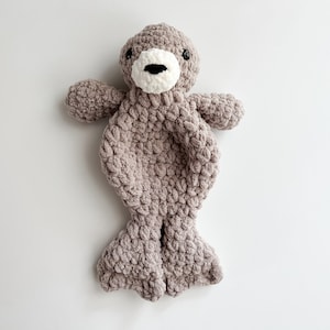 May include: A grey crocheted plush toy shaped like a seal with white felt eyes and a white felt nose.