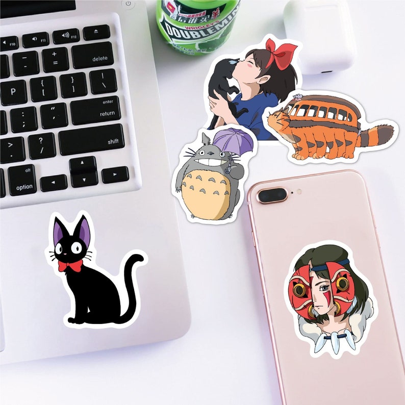 May include: A set of nine stickers featuring characters from the animated film Studio Ghibli. The stickers are printed on white glossy paper and feature a black cat, a grey furry creature with a large nose, a girl with brown hair and a red dress, a cat-like creature with a red bow, a flying creature with a red mask, and a yellow and orange creature with a red roof.