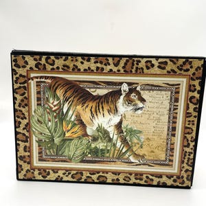 May include: A rectangular decorative plaque featuring a central image of a tiger walking through tropical foliage against a vintage map background. The image is framed by a border with a brown and black leopard print pattern on a tan background.