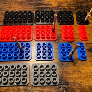 May include: A set of nine different colored plastic storage trays with multiple small round holes. Each tray has a different color, including black, red, blue, and gray. Some trays have reeds inserted into the holes.