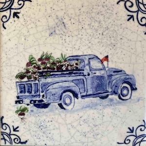 May include: A blue vintage pickup truck with a white bed is filled with a large harvest of red beets. The truck has a small American flag on the back. The image is painted on a white ceramic tile with a blue and white crackle glaze.