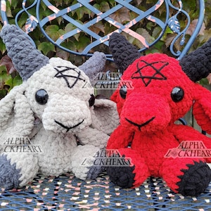 May include: Two plush goat toys, one gray and one red, with black horns and hooves. Each has a black pentagram on its head and the text "ALPHA LOCKHEART" on its body. They are sitting on a blue metal chair.