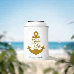 Może przedstawiać: Biała osłona na puszkę z złotym motywem kotwicy i napisem "Bride's Mate". Poniżej kotwicy znajduje się napis "Custom Words". Tło przedstawia scenę plażową z błękitną wodą i niebem.